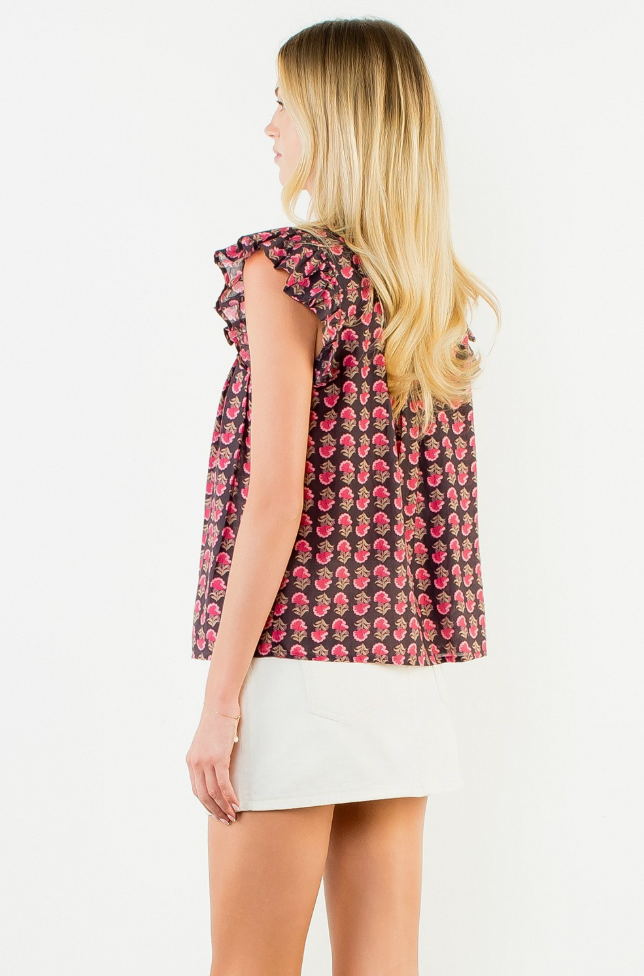 A woman shown from the back wearing a sleeveless top with a pink and red floral pattern on a dark background, paired with a white mini skirt, against a plain white studio background.