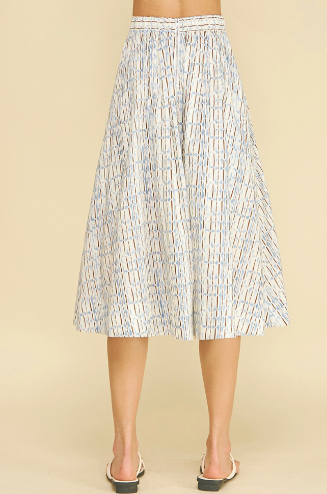 A pleated A-line midi skirt with a white base and vertical blue and gray stripe pattern, shown on a model from the back against a solid beige background.