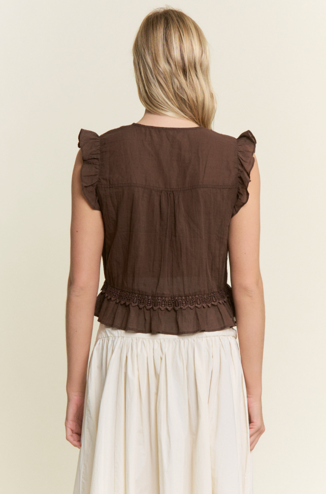 A woman shown from the back wearing a dark brown sleeveless ruffled top and a cream-colored skirt, against a plain light beige background.