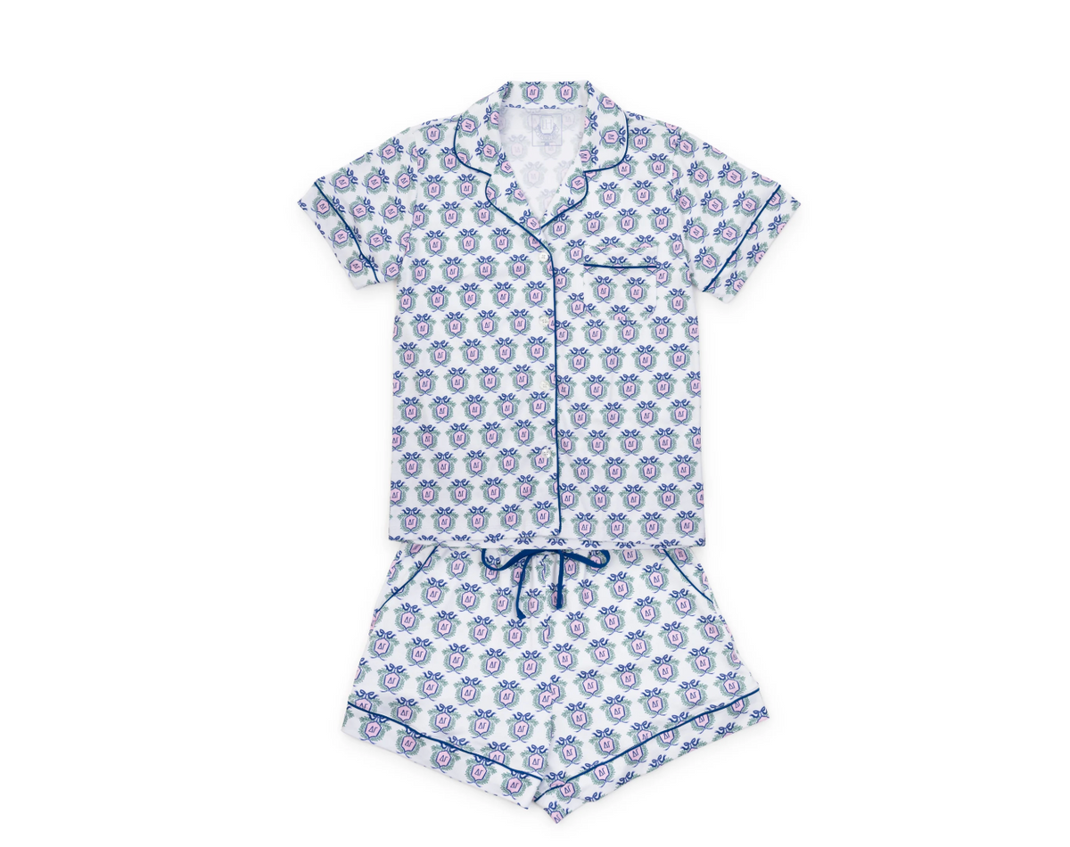 A two-piece women's pajama set featuring a short-sleeve button-front top and matching shorts, both in a white fabric with a repeating blue and purple floral pattern and blue piping details.