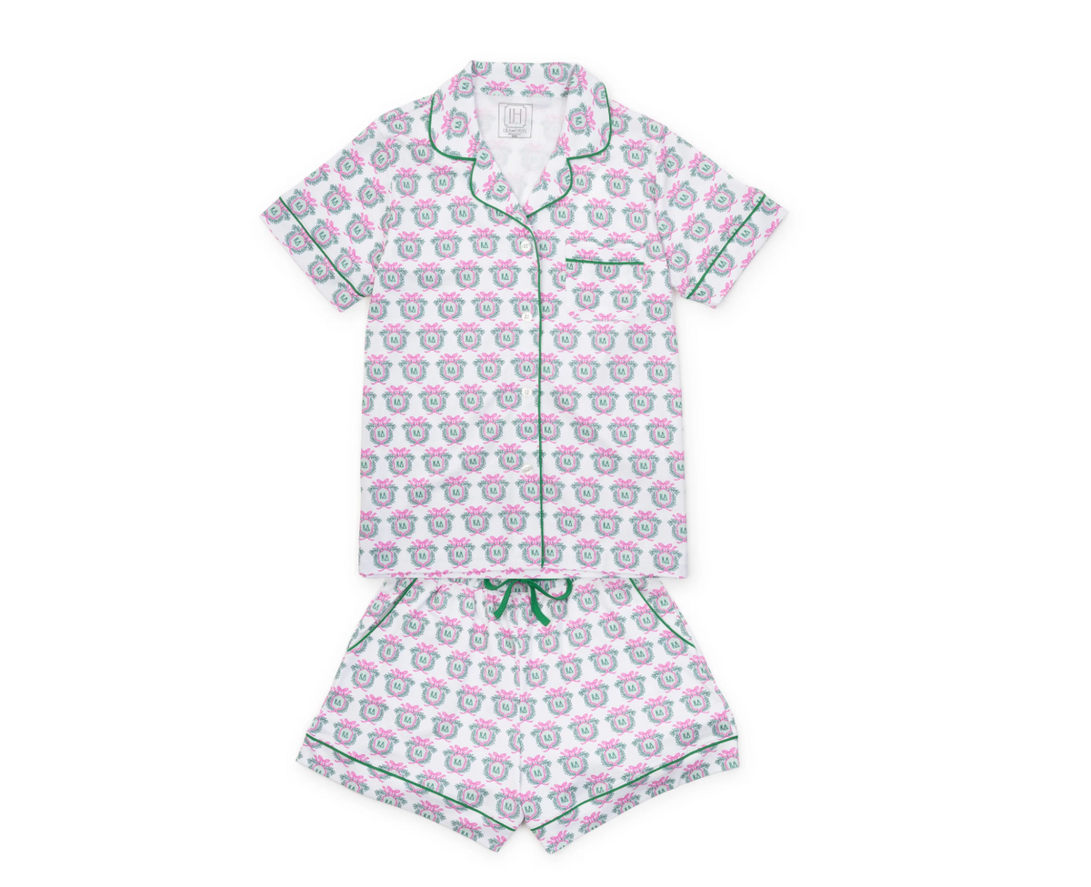 A two-piece short-sleeve pajama set featuring a white base with a repeating pink and green cartoon face pattern, complete with green piping and a matching green drawstring.
