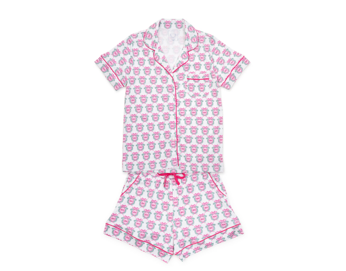 A two-piece women's pajama set featuring a short-sleeve button-up top and matching shorts. The pajamas are white with a repeating pattern of pink cartoon cupids and pink piping details, including the collar, sleeve edges, and waist tie.