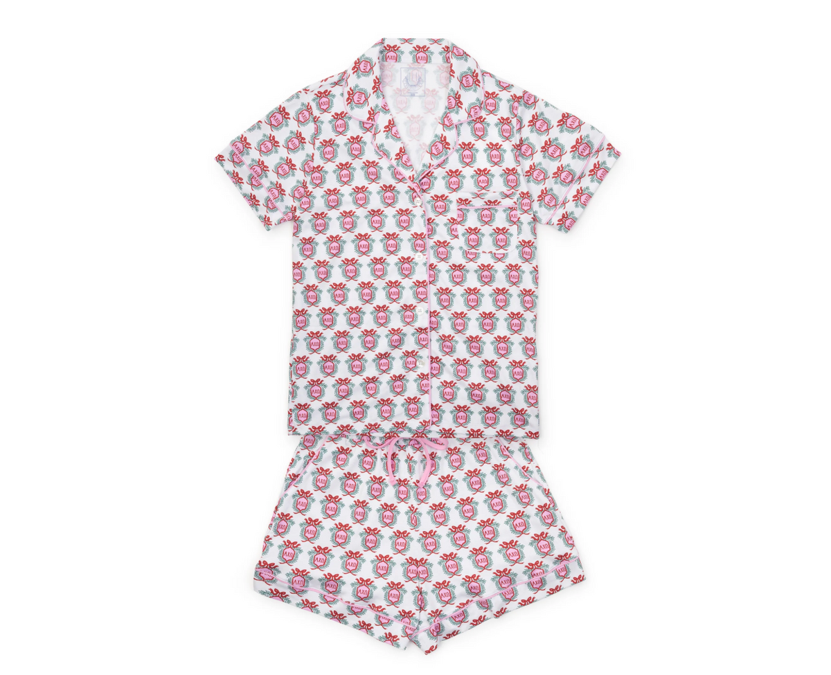 A two-piece children's pajama set consisting of a short-sleeve button-up shirt and matching shorts, both featuring an all-over repeating pattern of pink cartoon characters on a white background.