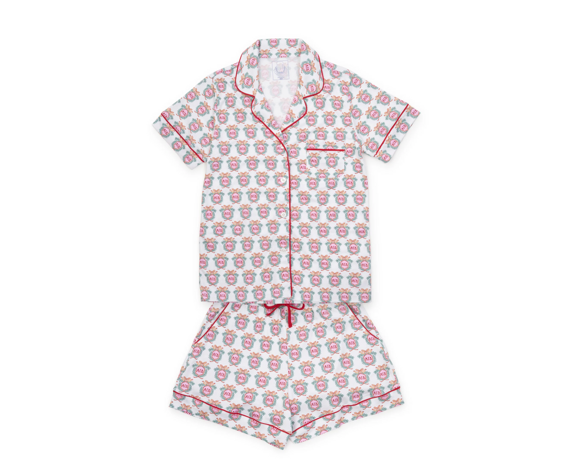 A two-piece short-sleeve pajama set laid flat on a white background, featuring a white base with a repeating red and gray graphic pattern and red piping trim.