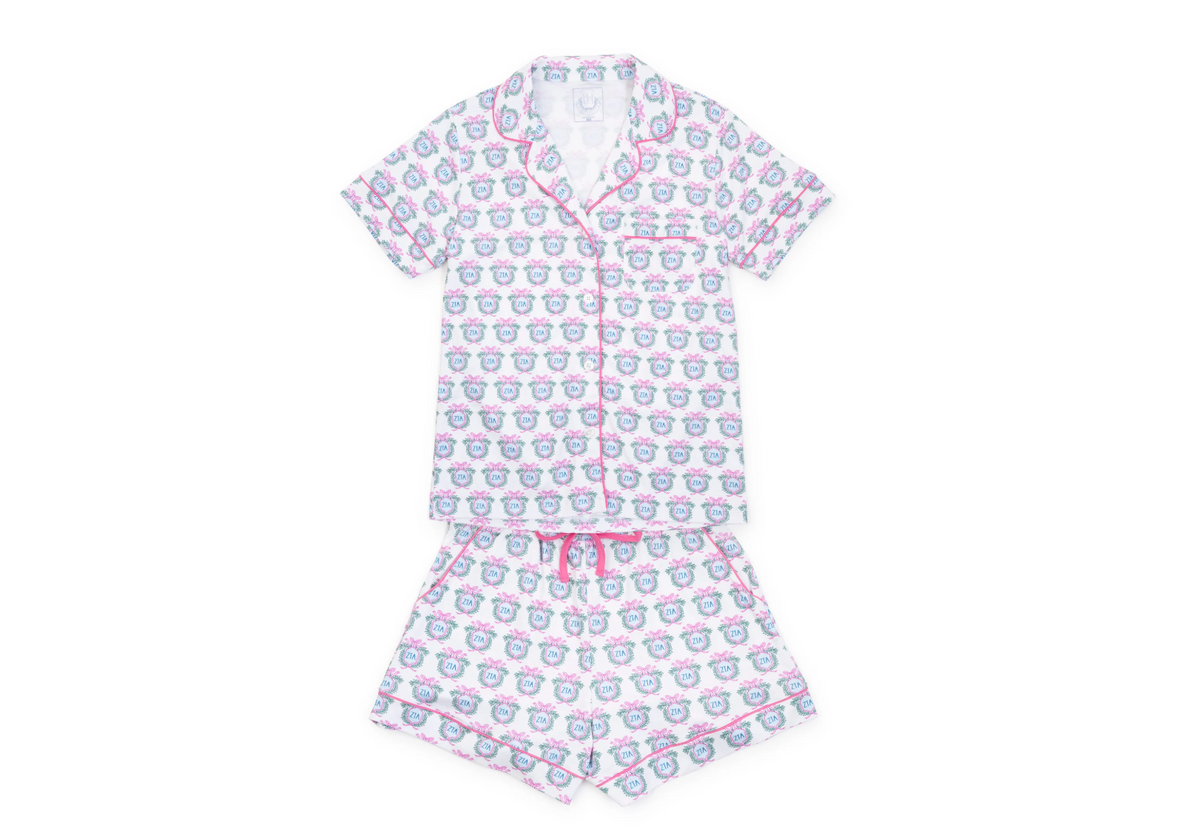A two-piece short-sleeve pajama set with a white base, featuring an all-over repeating pattern of cartoon cupids and pink piping details, laid flat on a white background.
