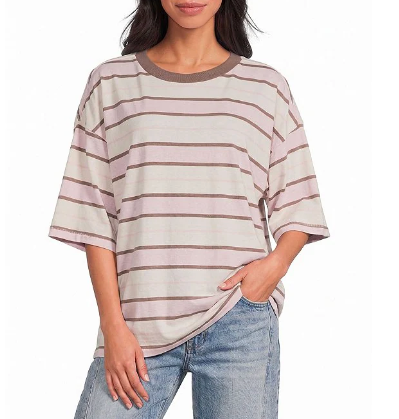 A woman wearing an oversized short-sleeve striped t-shirt with horizontal bands of dusty pink, beige, and brown, paired with light-wash blue jeans against a plain white background.