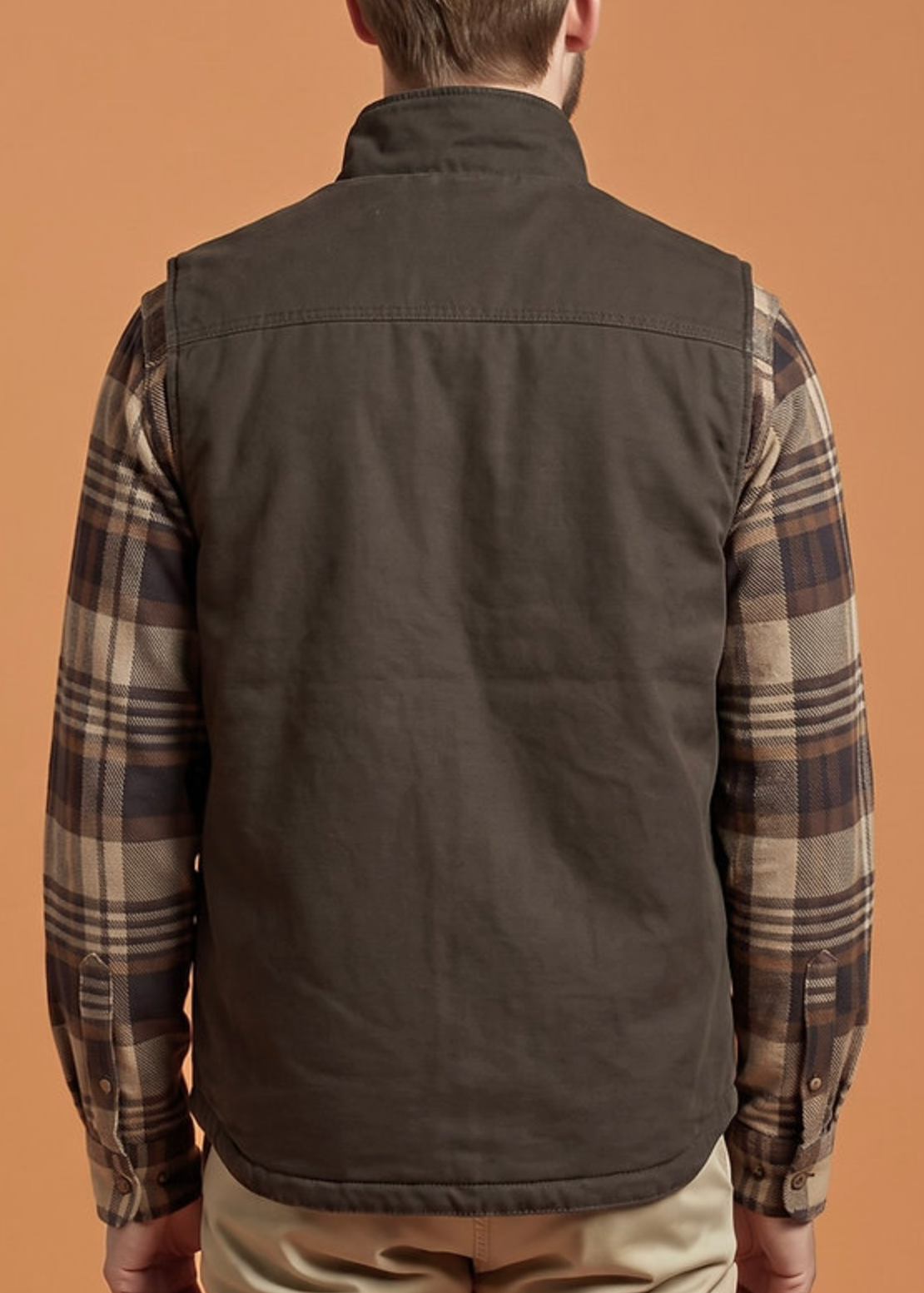 A man shown from the back wearing a dark brown zip-front vest over a brown and beige plaid flannel shirt, standing against a solid warm brown background.