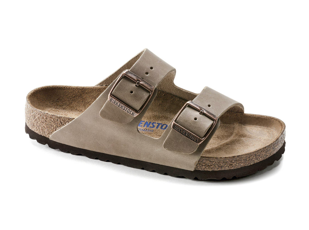 A single double-strap sandal in a taupe-gray color, featuring a suede-like upper, adjustable double straps with metal buckles, a cork-look midsole, and a black outsole. The brand name 'ENSTO' is visible on the insole.