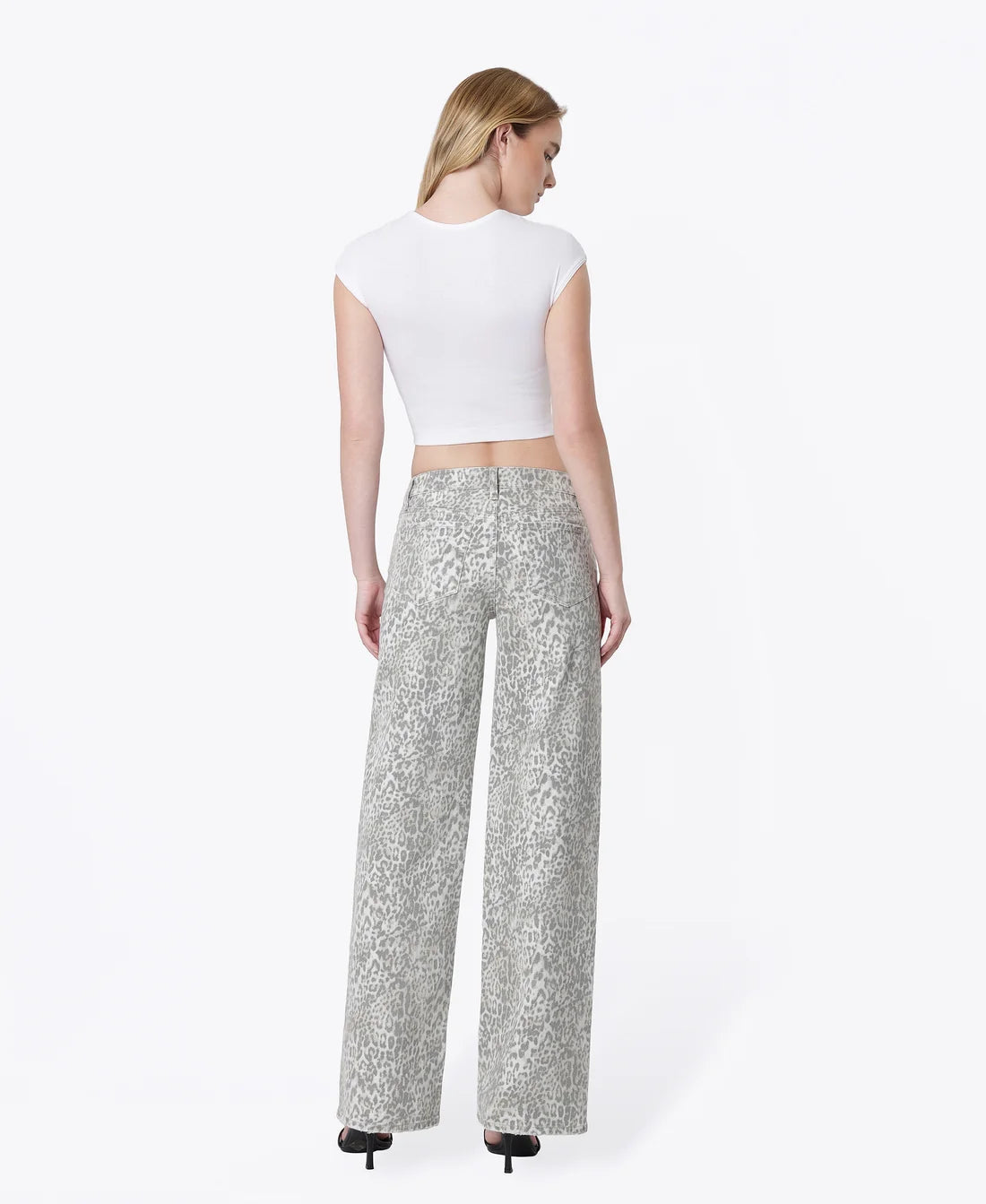 A woman shown from the back wearing a white cropped short-sleeve top and high-waisted, wide-leg trousers with a silver and gray animal print, paired with black heels, against a plain white studio background.