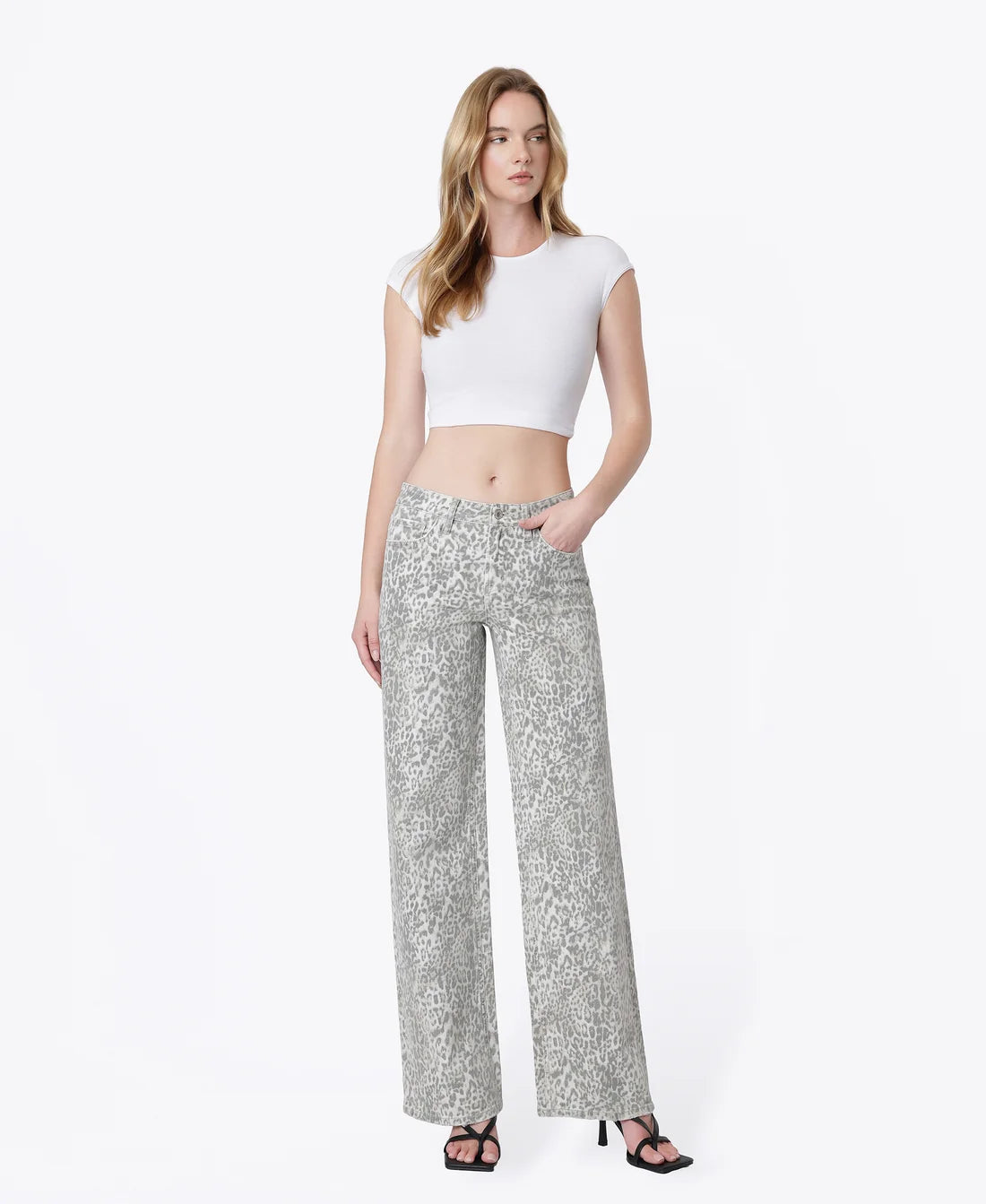 A woman modeling a white short-sleeve crop top and light gray wide-leg trousers with a subtle floral pattern, standing against a plain white studio background.