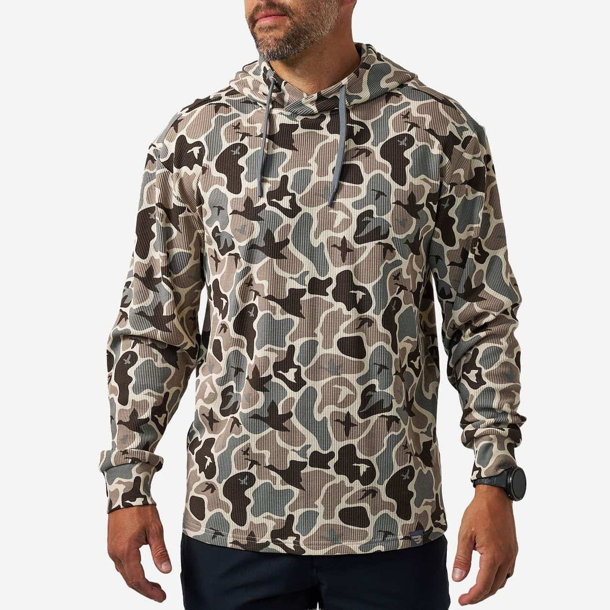 A man wearing a camouflage hooded sweatshirt with a kangaroo pocket, shown from the waist up against a light gray studio background.