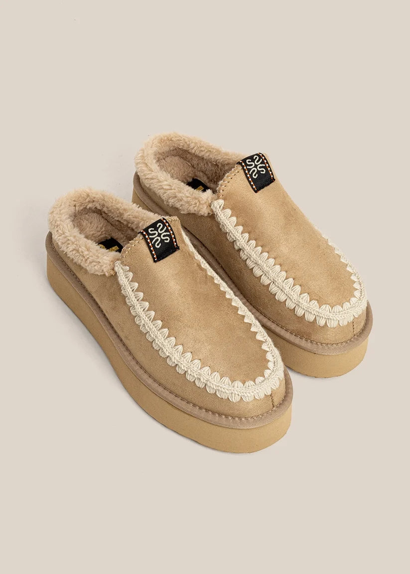 Pair of tan slippers with white trim on a beige background