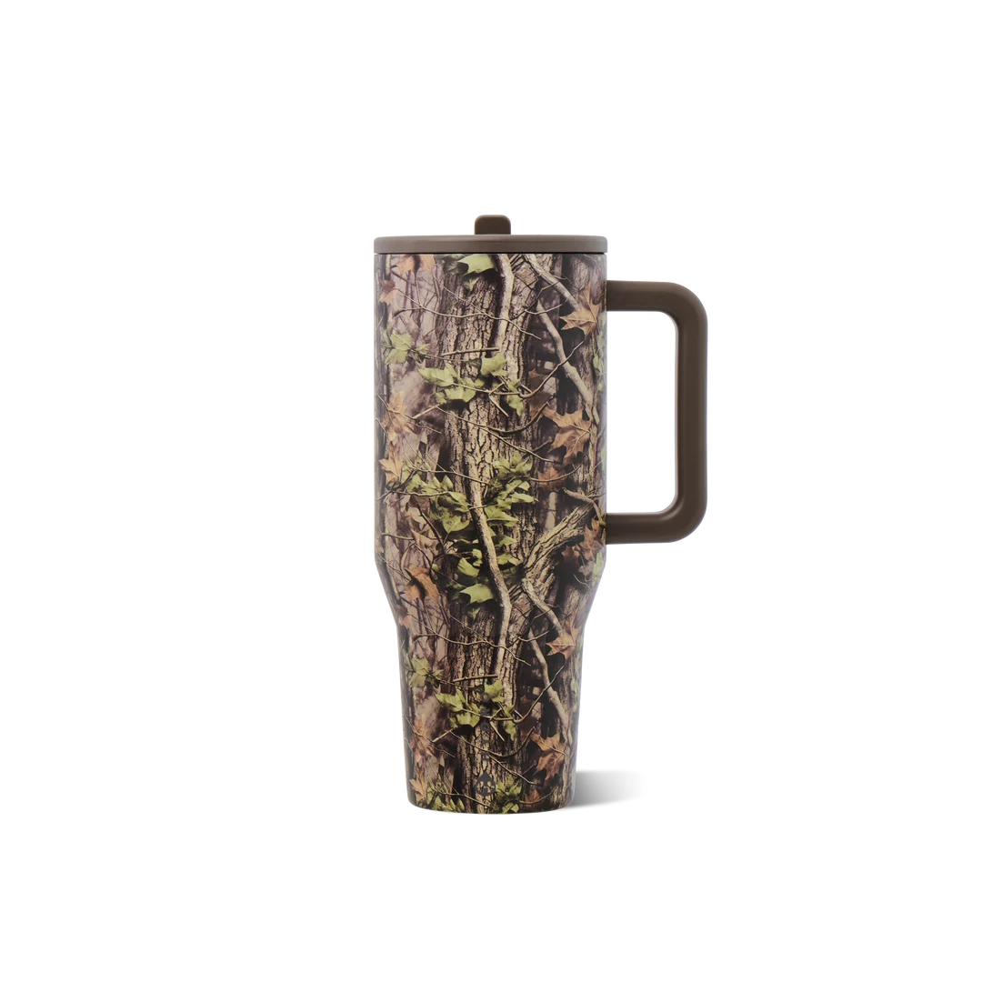 A tall insulated travel mug with a lid and handle, featuring a realistic brown and green tree bark camouflage pattern, shown on a plain white background.