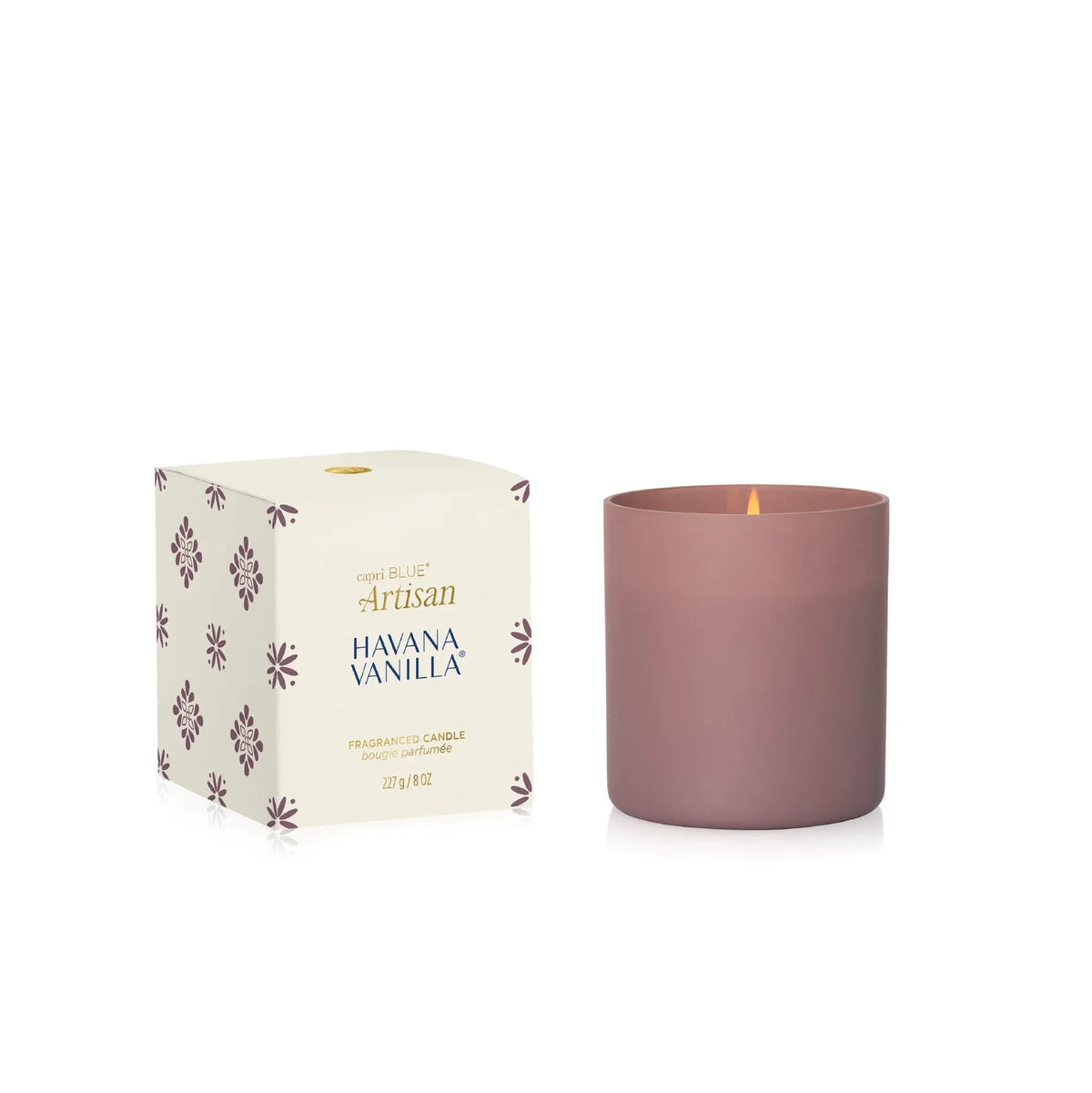 A matte dusty rose candle in a cylindrical glass vessel next to its cream-colored packaging box, which features purple floral patterns and gold and blue text reading 'Luna Blue Artisan Havana Vanilla'.