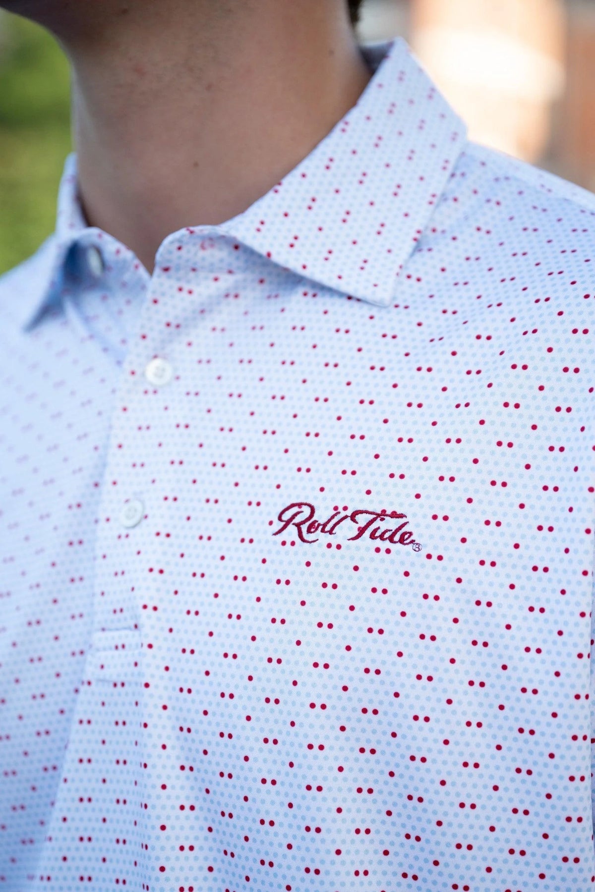 Close-up of a person wearing a white short-sleeve collared button-up shirt with a red micro-dot pattern and a red embroidered 'Roll Tide' logo on the chest.