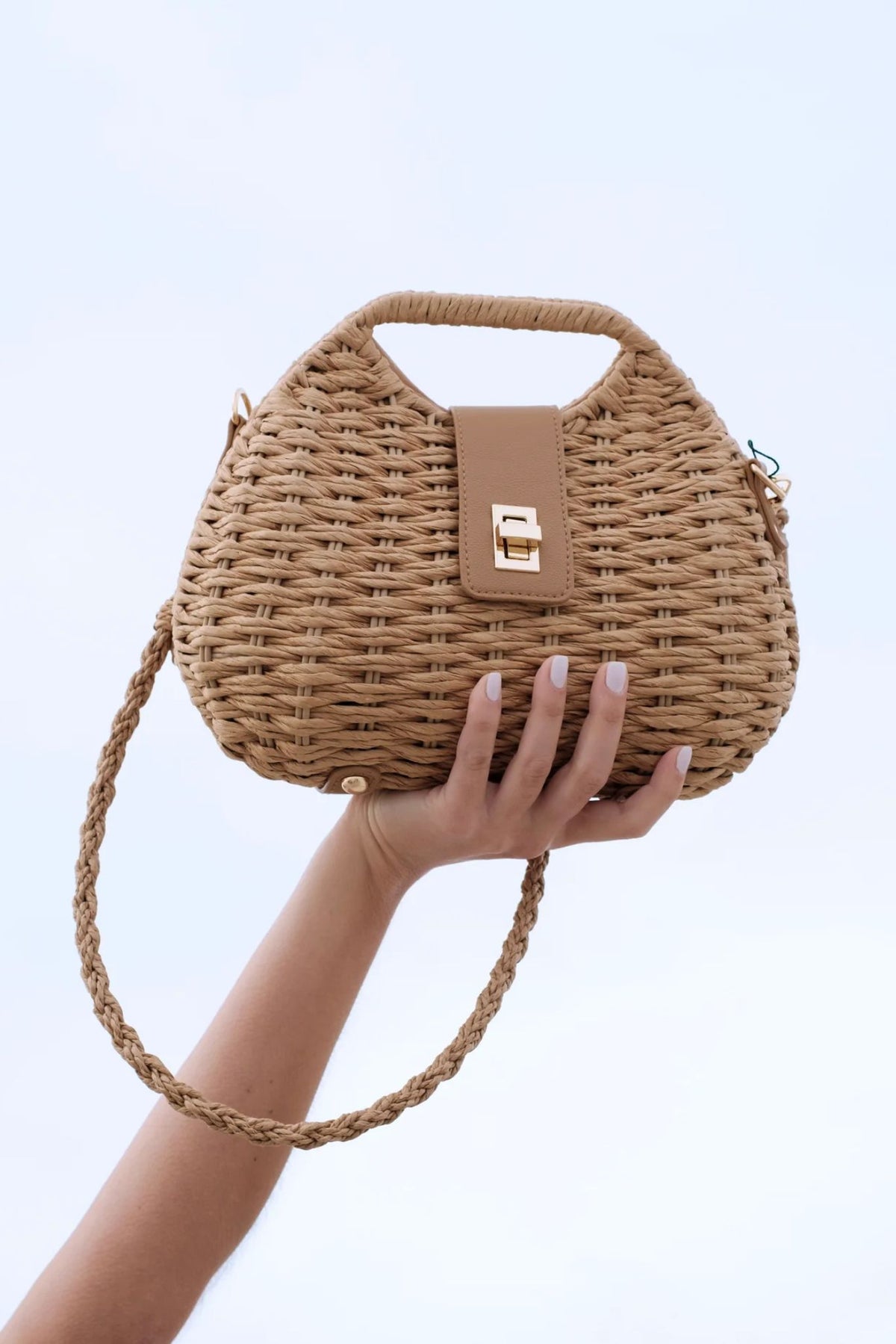 Hand holding a woven handbag against a light blue background