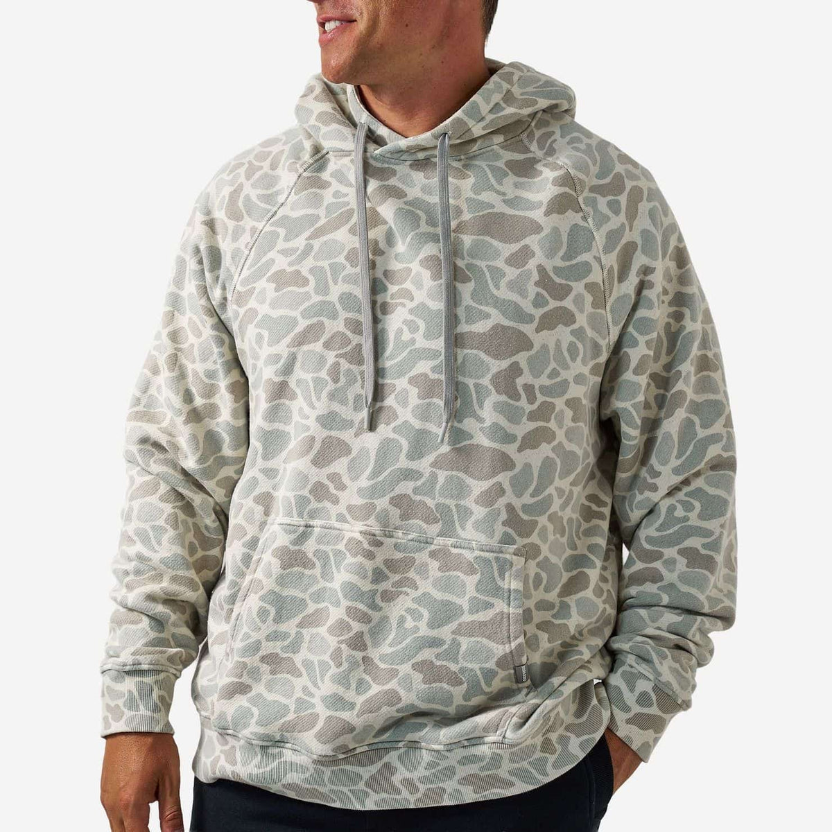 A man wearing a light gray and beige animal-print hoodie with a kangaroo pocket, shown from the chest down against a plain light gray background.