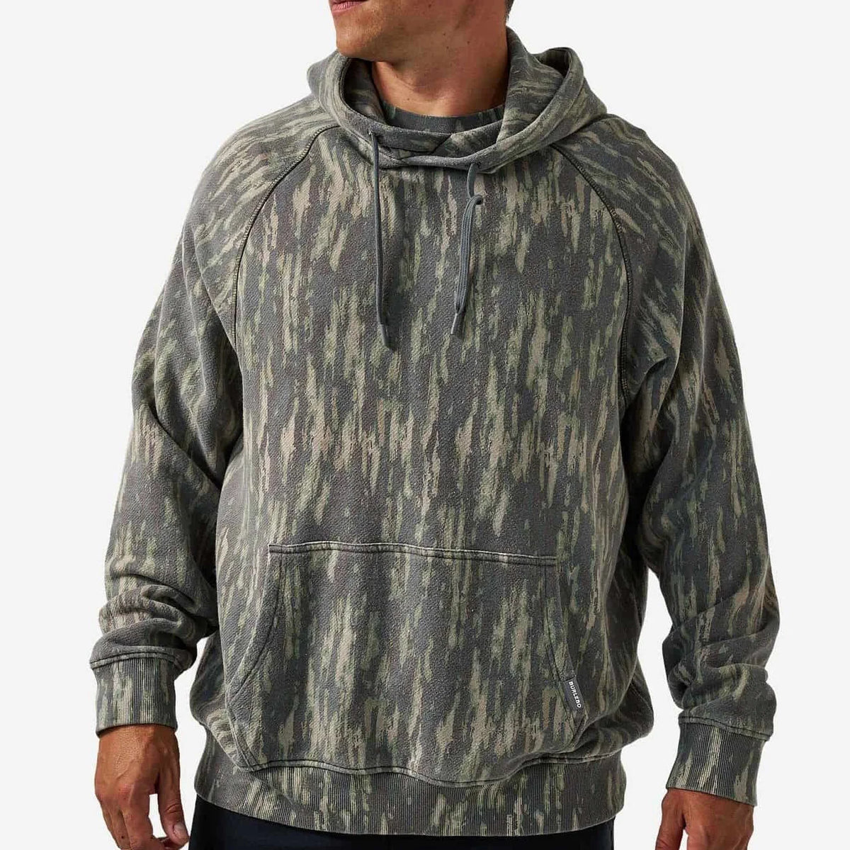 A man wearing a camouflage-patterned pullover hoodie with a drawstring hood and kangaroo pocket, shown from the waist up against a light gray background.