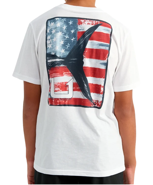 A child viewed from the back wearing a white short-sleeve T-shirt with a large rectangular graphic on the back featuring a distressed American flag and a dark abstract shape.