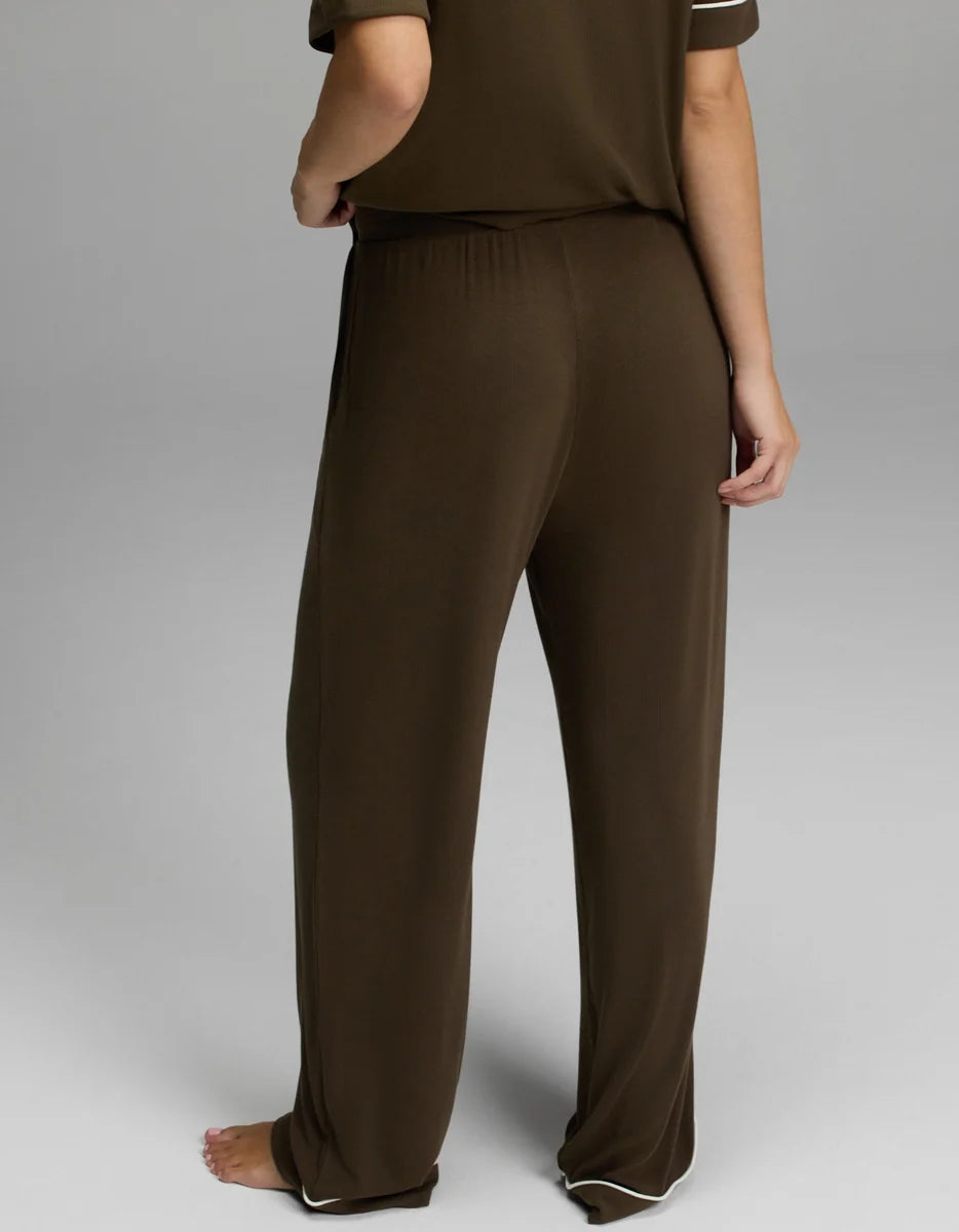 A person shown from the back wearing loose brown lounge pants and a matching brown top, photographed against a light gray studio background.