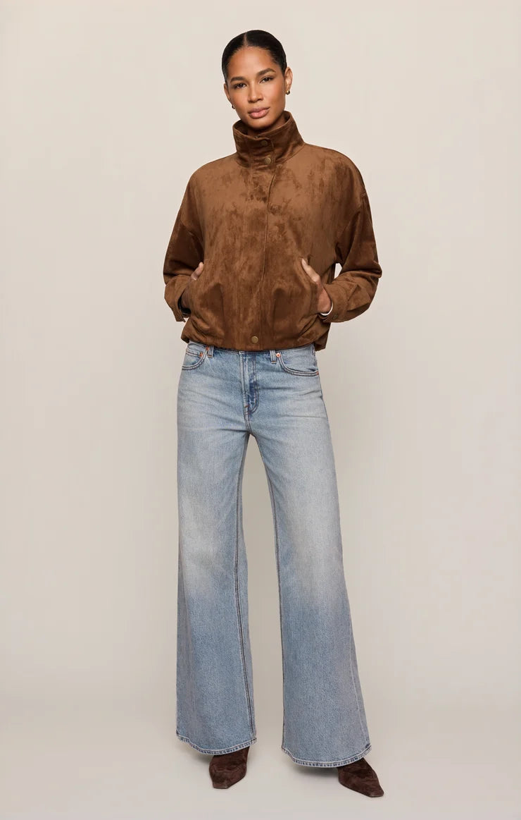 woman standing against a white background with a tan fully zipped up jacket and jeans