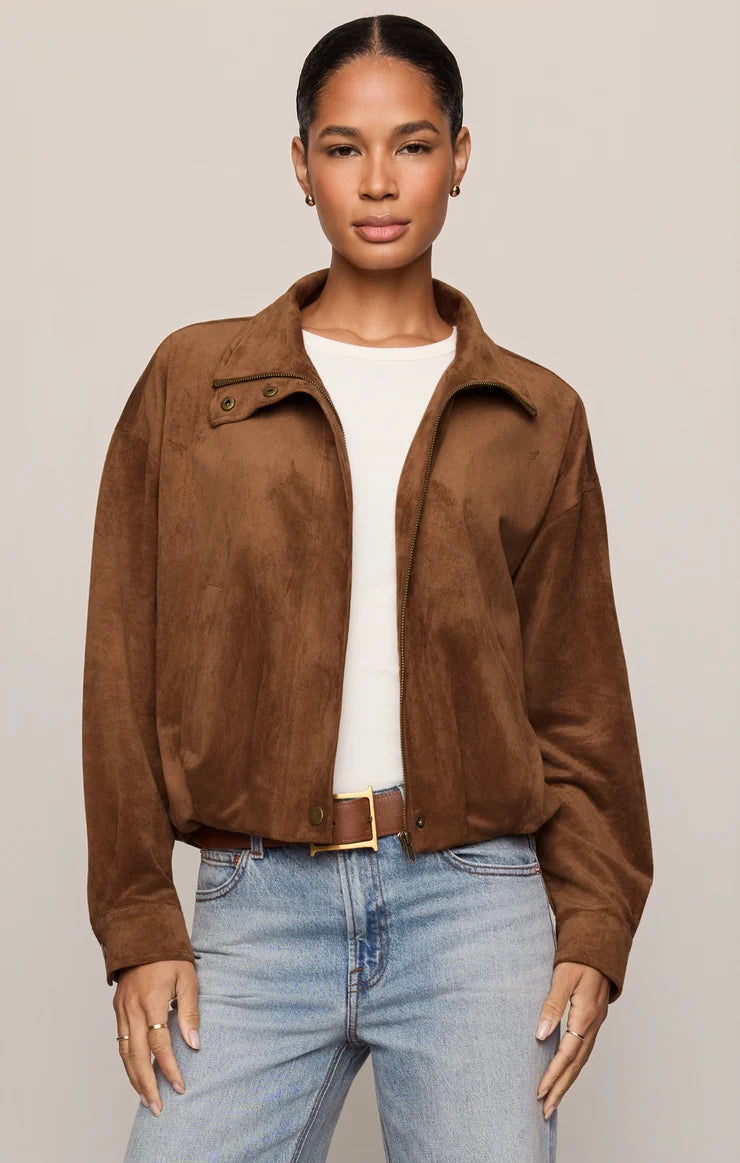 woman modeling a tan suede zip up jacket with jeans and belt. on a plain background 