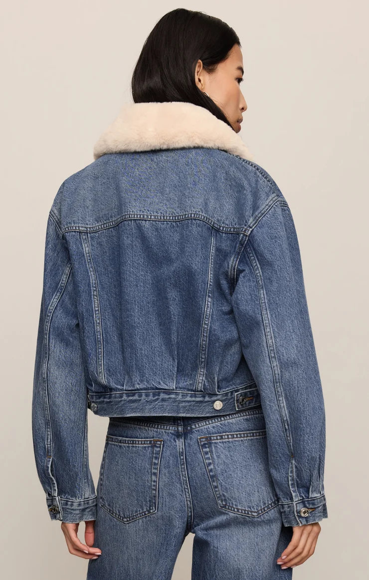 Denim jacket with fur collar worn by a person on a plain background