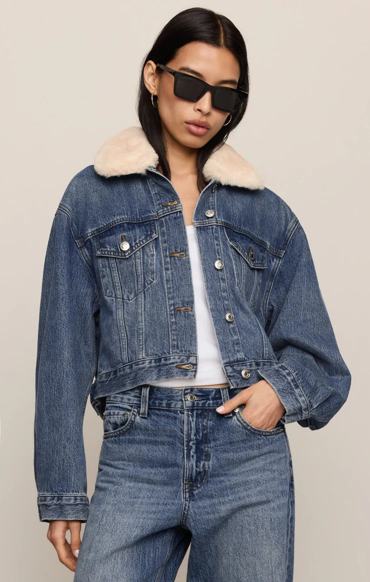 Woman wearing a denim jacket with fur collar and jeans on a beige background