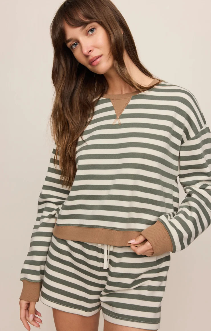 A woman wearing a matching striped lounge set consisting of a long-sleeve cropped top and shorts. The set features horizontal sage green and cream stripes with solid sage green ribbed trim at the split neckline, cuffs, and hem.