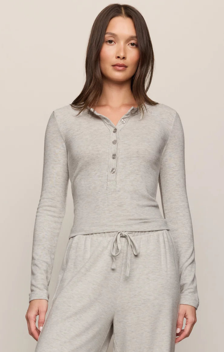 A woman modeling a light heather gray long-sleeve henley top with matching drawstring sweatpants against a plain beige studio background.