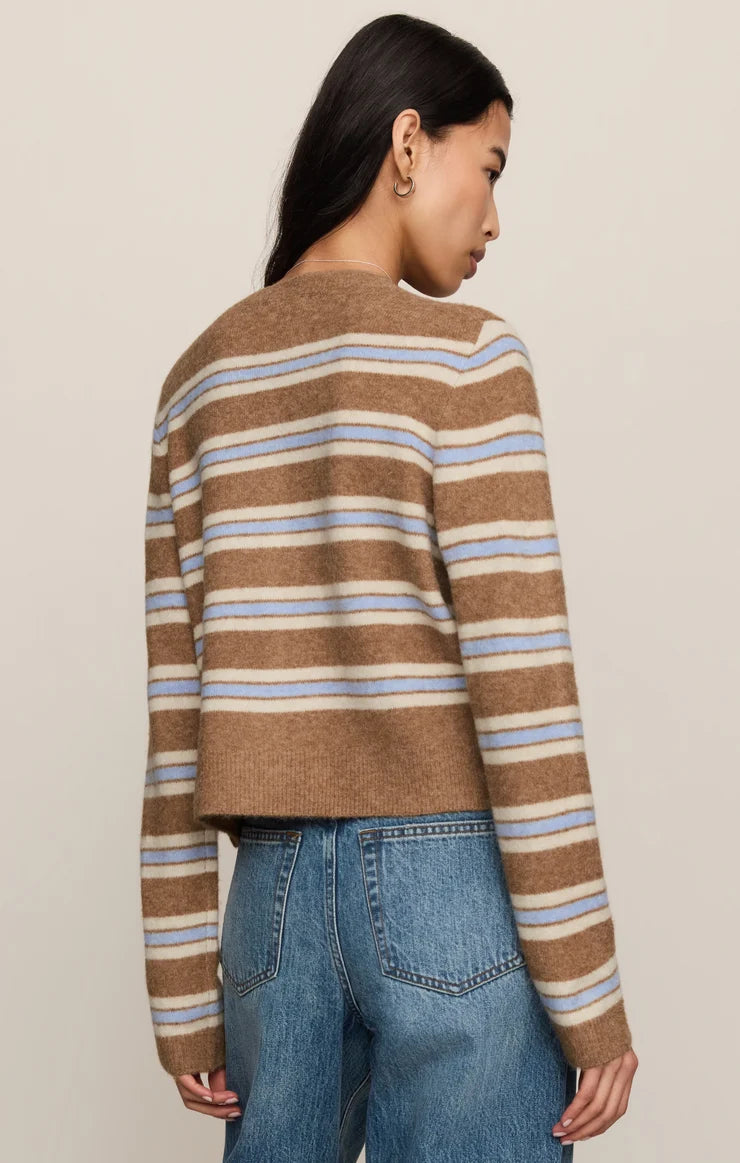 A woman shown from the back wearing a cropped knit sweater with horizontal stripes in brown, beige, and light blue, paired with blue jeans, against a plain light beige studio background.