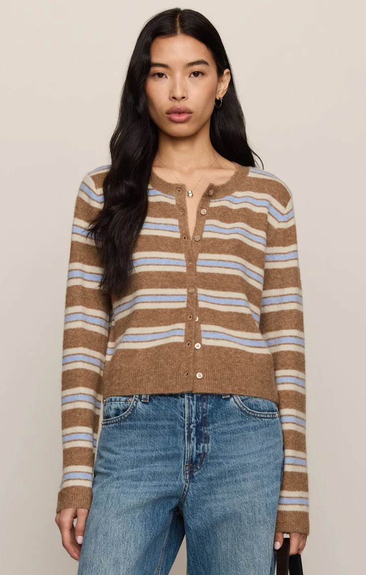 A woman modeling a cropped, long-sleeve knit cardigan with horizontal brown, beige, and light blue stripes, paired with blue jeans against a solid light beige background.