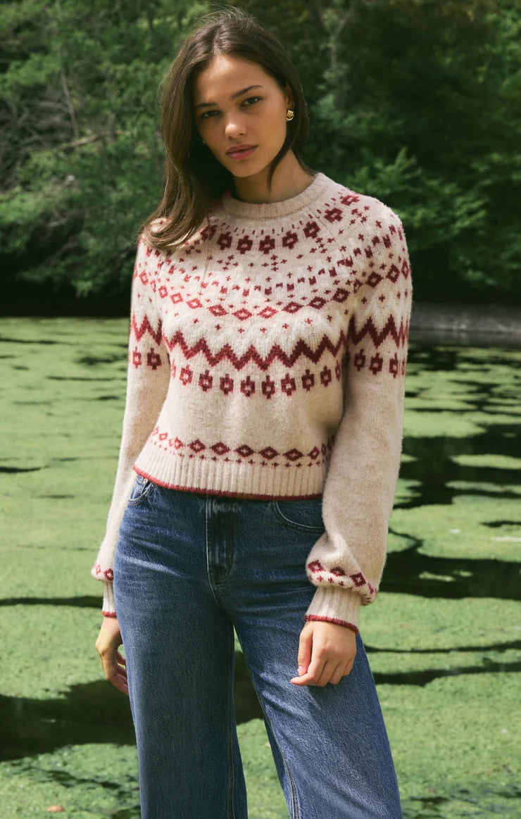 woman standing in front of lake wearing a tan sweater and jeans
