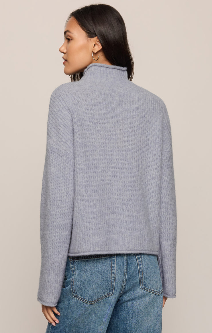 Woman wearing a gray textured sweater and blue jeans on a beige background