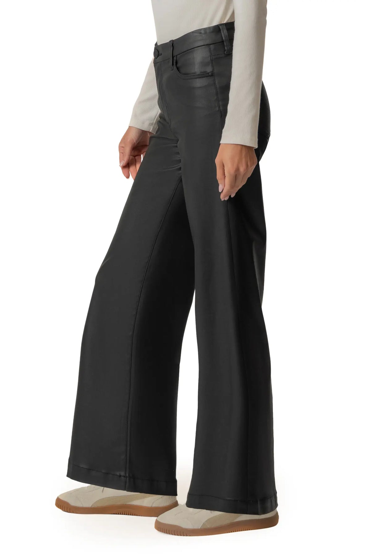 A model wearing black wide-leg pants with a faux-leather finish, styled with a cream long-sleeve top and beige slip-on shoes against a white background.