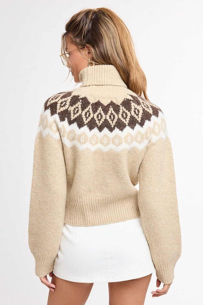 A woman shown from the back wearing a cropped knit sweater with a cream base, white and dark brown Fair Isle pattern across the shoulders and upper back, and a white mini skirt against a plain white studio background.