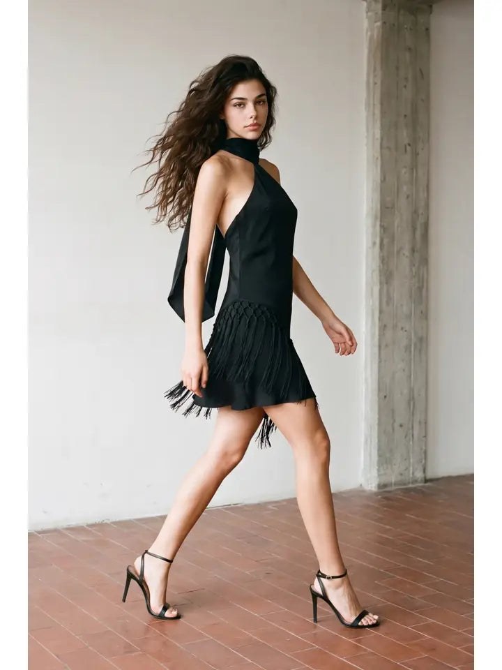 Woman standing in front of white wall wearing a black mini dress