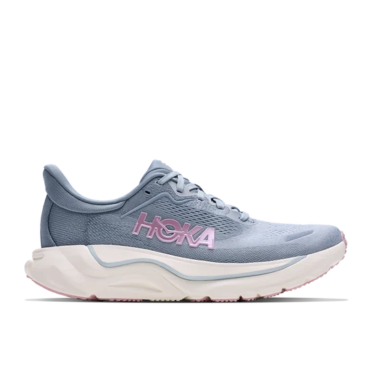 A HOKA running shoe in light blue with a pink HOKA logo on the side, featuring a thick white and light blue midsole with a pink outsole edge, shown against a plain white background.
