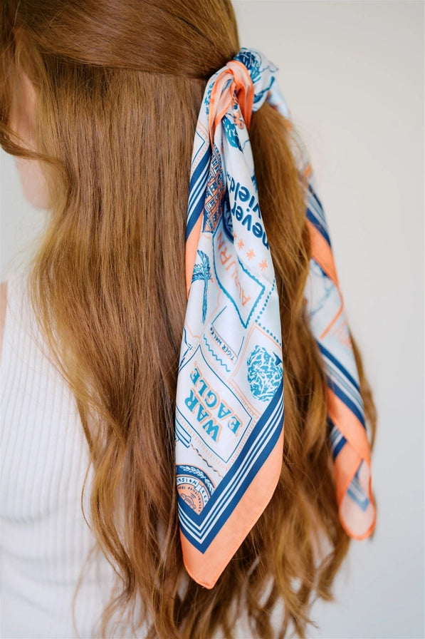 Woman with long brown hair wearing a patterned orange and blue hair scarf.