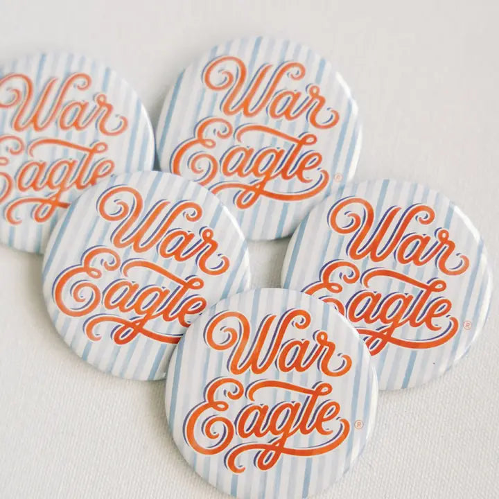 Five round buttons with a white and light blue striped background and orange cursive 'War Eagle' lettering, arranged on a light fabric surface.
