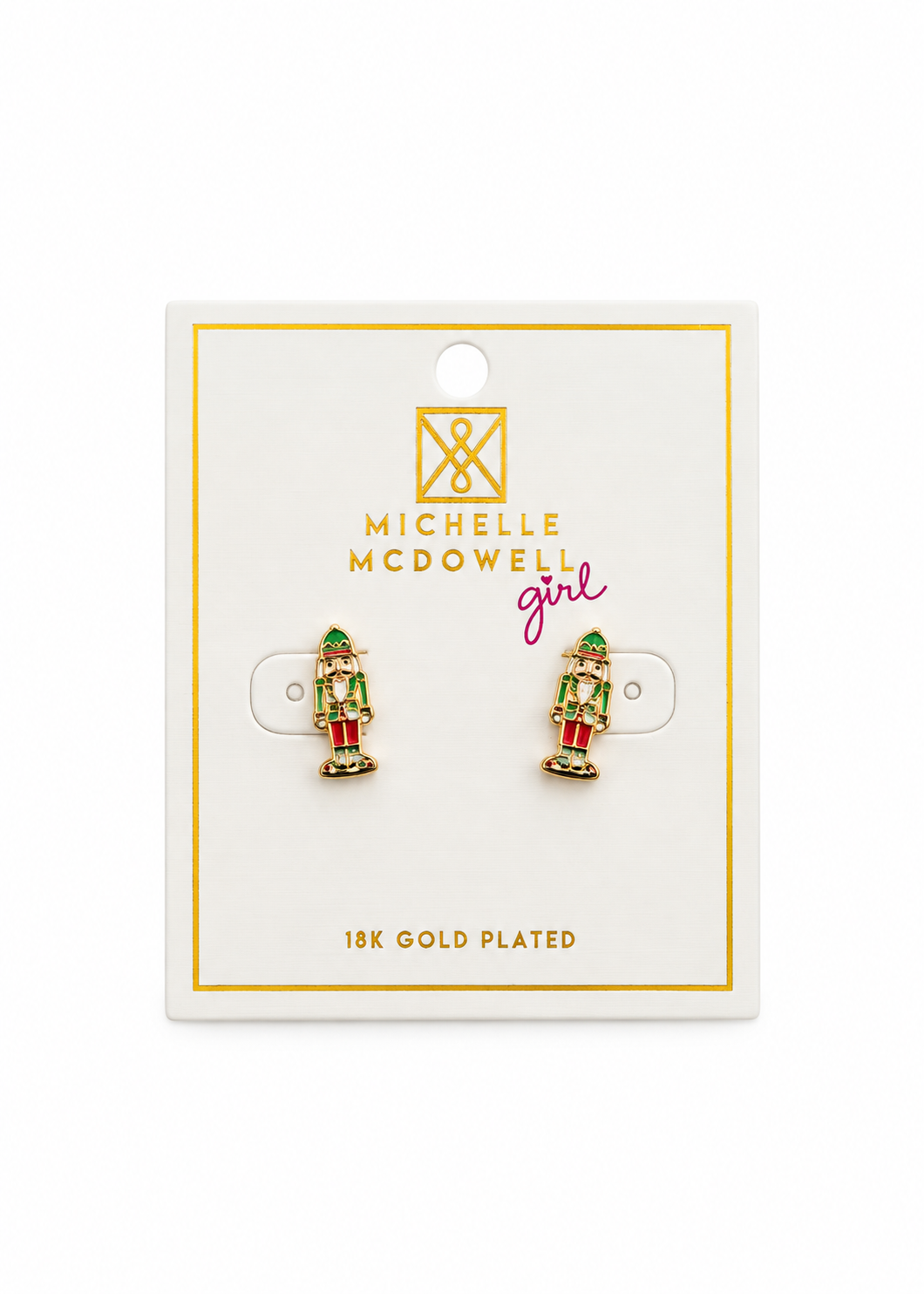 A pair of Michelle McDowell nutcracker stud earrings on a white display card with gold borders and text. The earrings are gold-plated with green, red, and white enamel detailing.