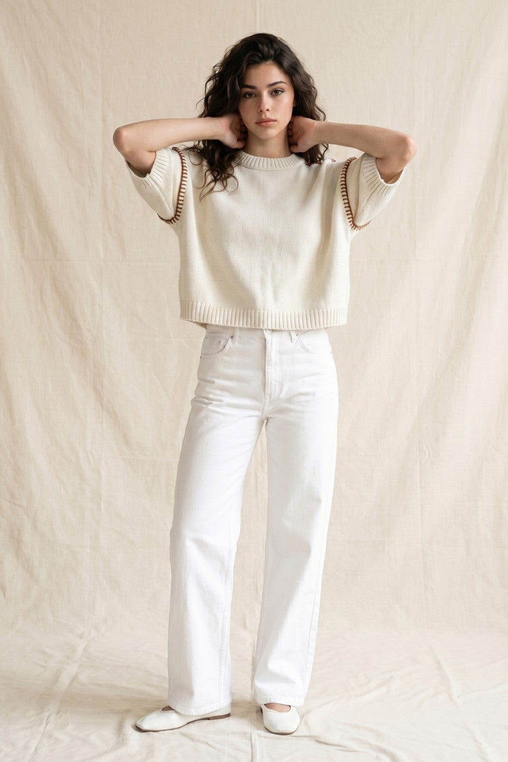Woman wearing a white sweater and pants against a plain background