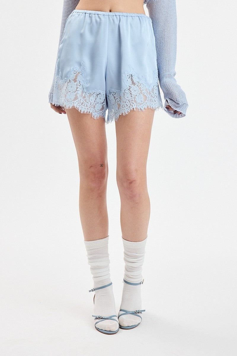 A model from the waist down wearing light blue shorts with a lace hem, white socks, and light blue high heels against a plain white studio background.