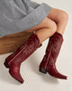 Red cowboy boots worn with a checkered dress on a neutral background