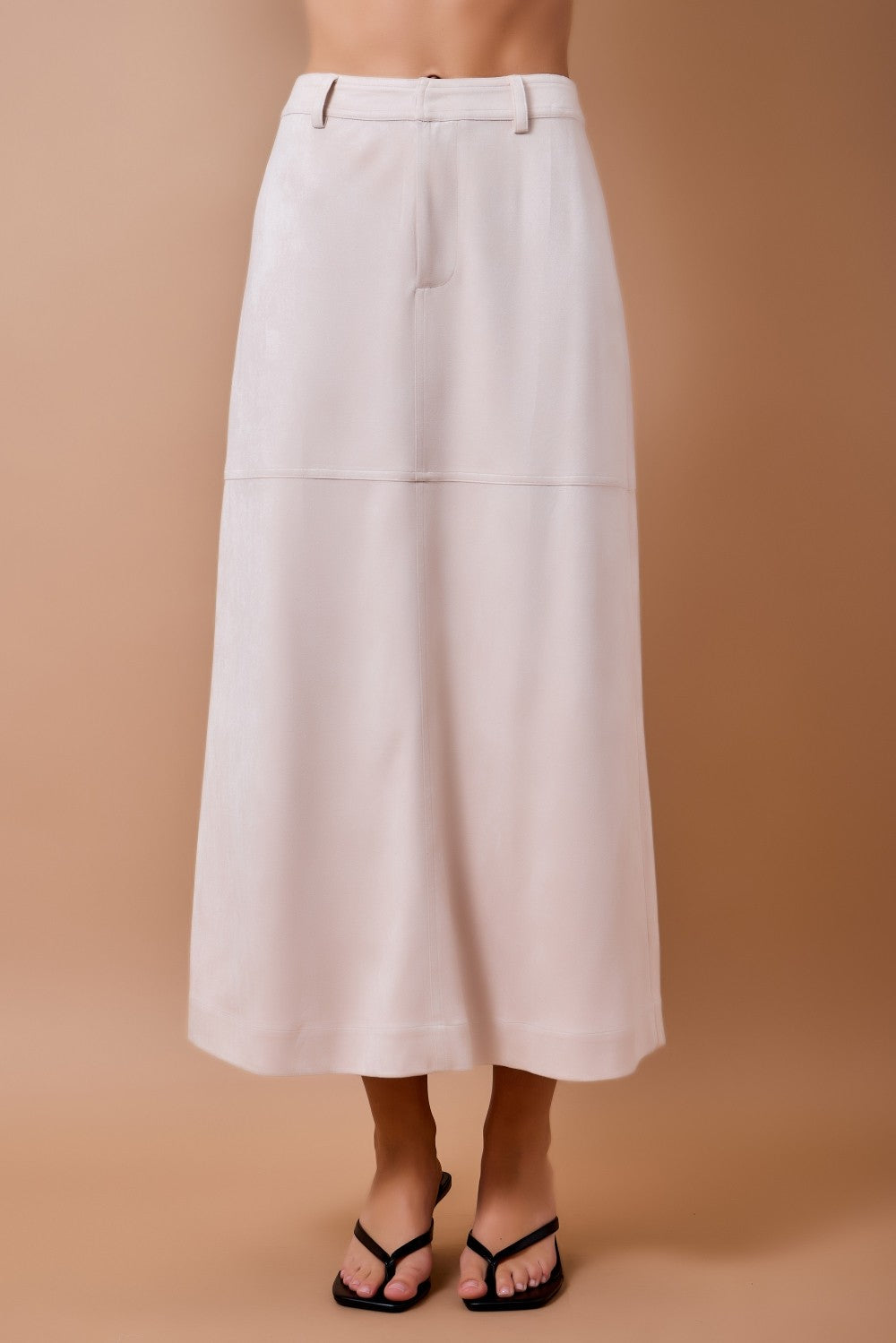 woman standing on tan background wearing cream suede skirt