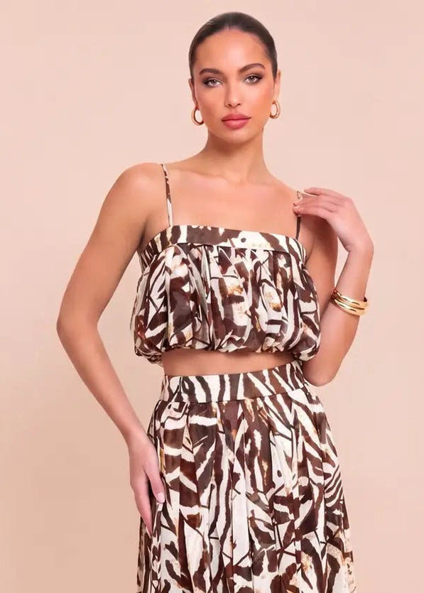 A woman modeling a two-piece matching set featuring a brown and beige abstract pattern, consisting of a strapless crop top and a high-waisted midi skirt, set against a solid beige background.