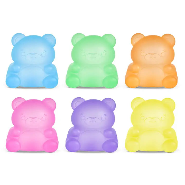 Six teddy bear-shaped glow-in-the-dark toys in pastel colors, arranged in two rows of three on a white background. The colors include light blue, light green, light orange, light pink, light purple, and light yellow.