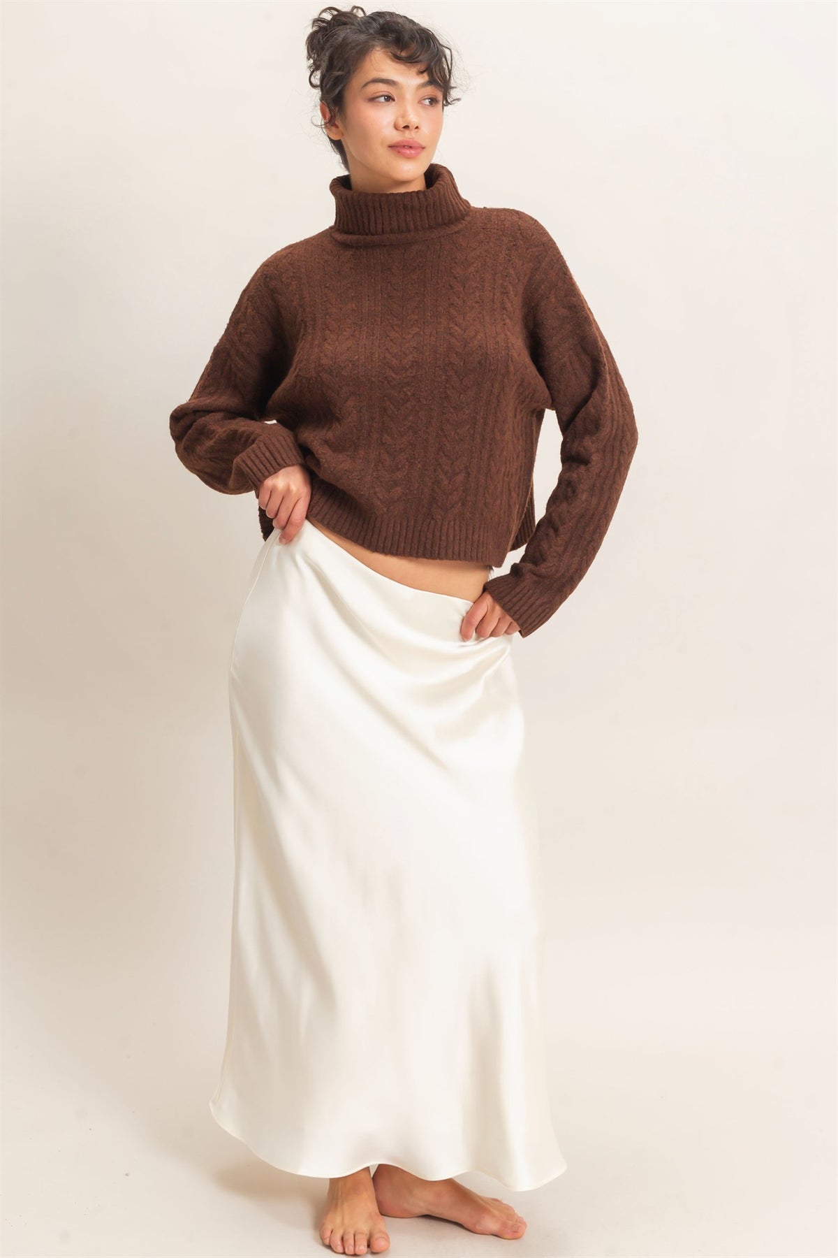 Person wearing a brown sweater and white skirt on a plain background