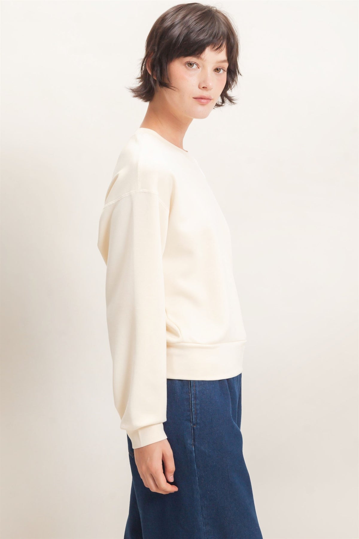 Person wearing a cream sweater and blue pants on a plain background