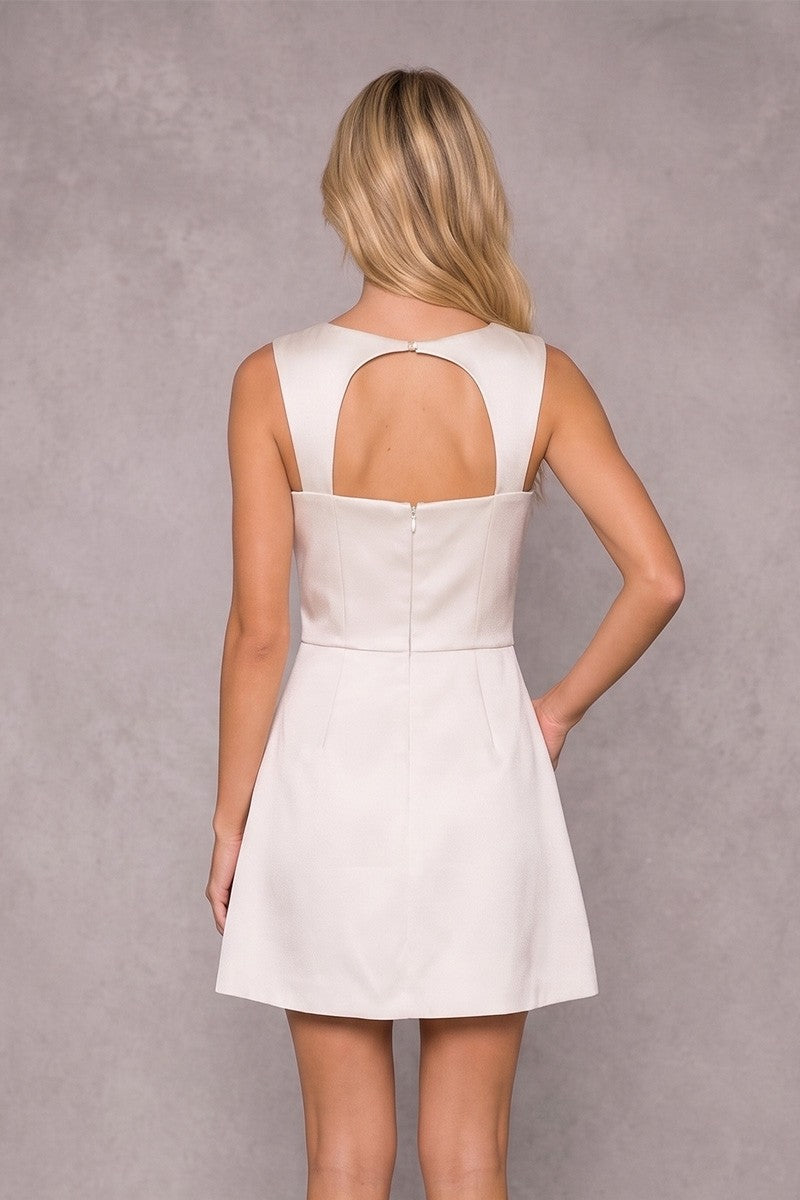 A woman shown from the back wearing a sleeveless white mini dress with a keyhole cutout at the upper back, photographed against a textured gray studio background.